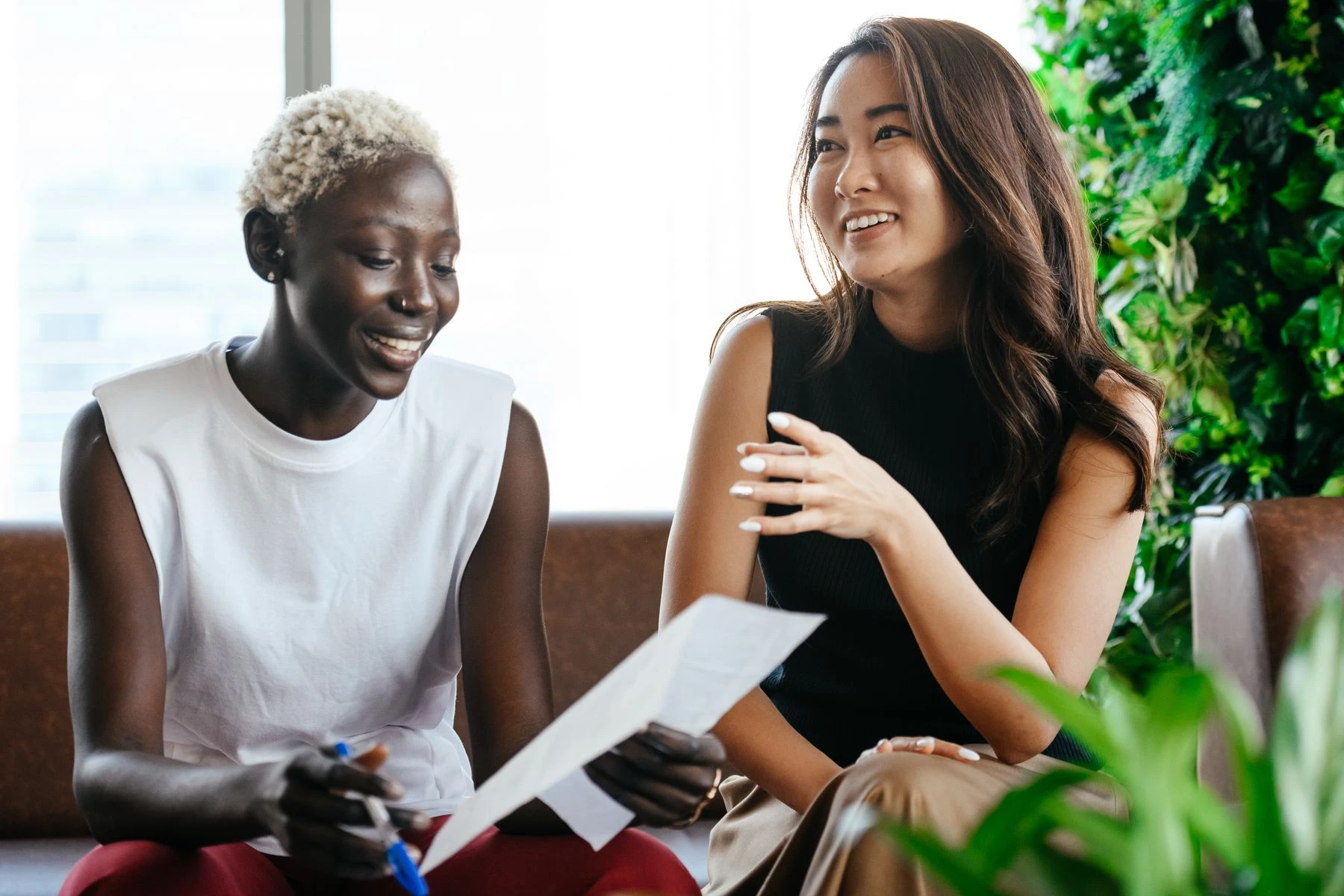 Two women smiling and talking together beside a bright window