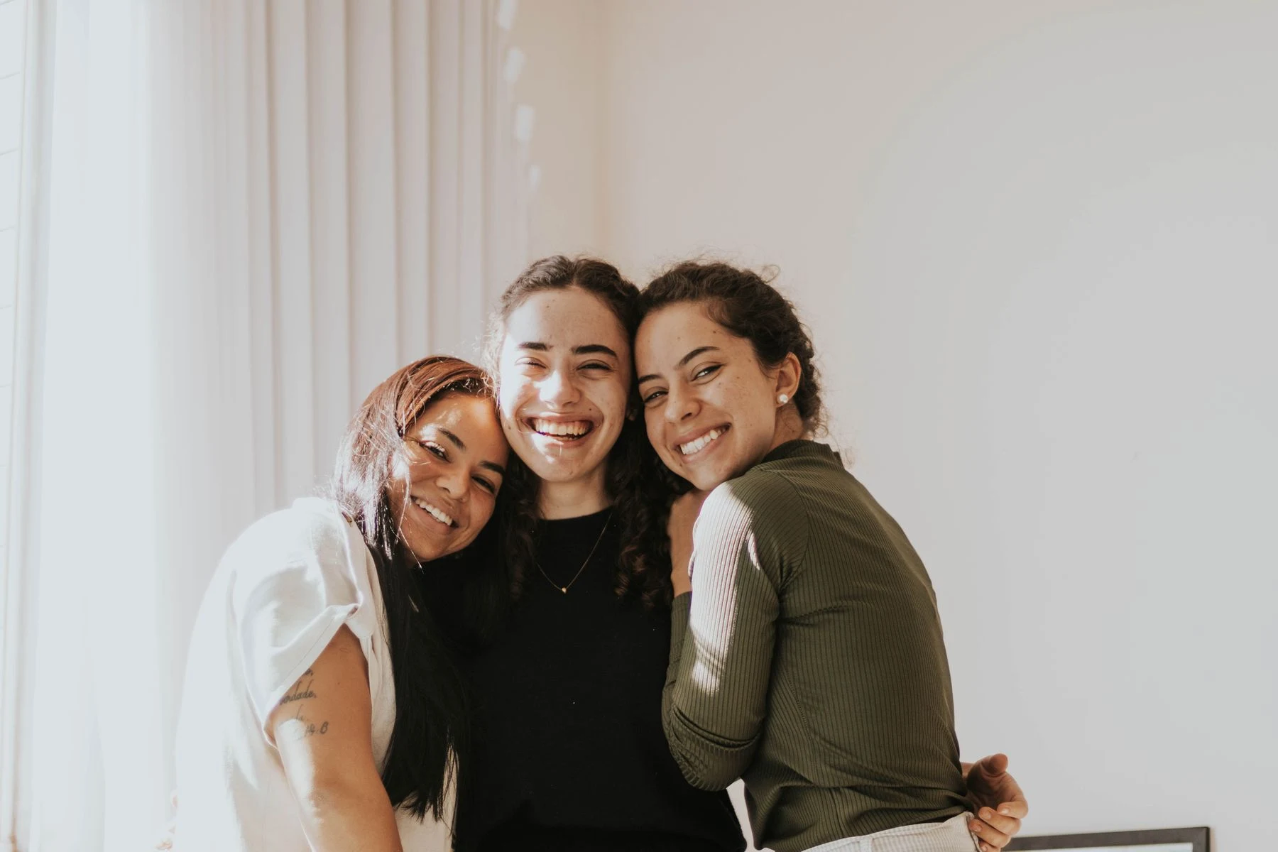 Three adults smiling and embracing in a sunlit room
