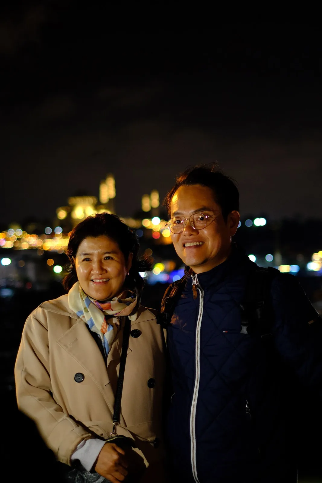 Smiling couple posing together under city lights at night.