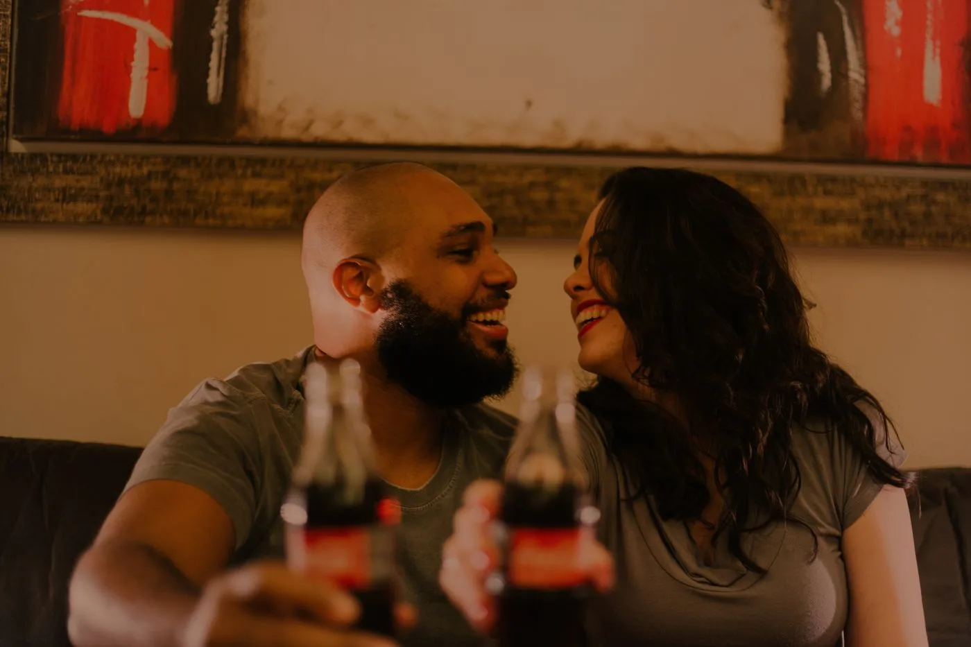 A joyful couple shares a soda and laughter indoors, capturing the essence of love and togetherness.