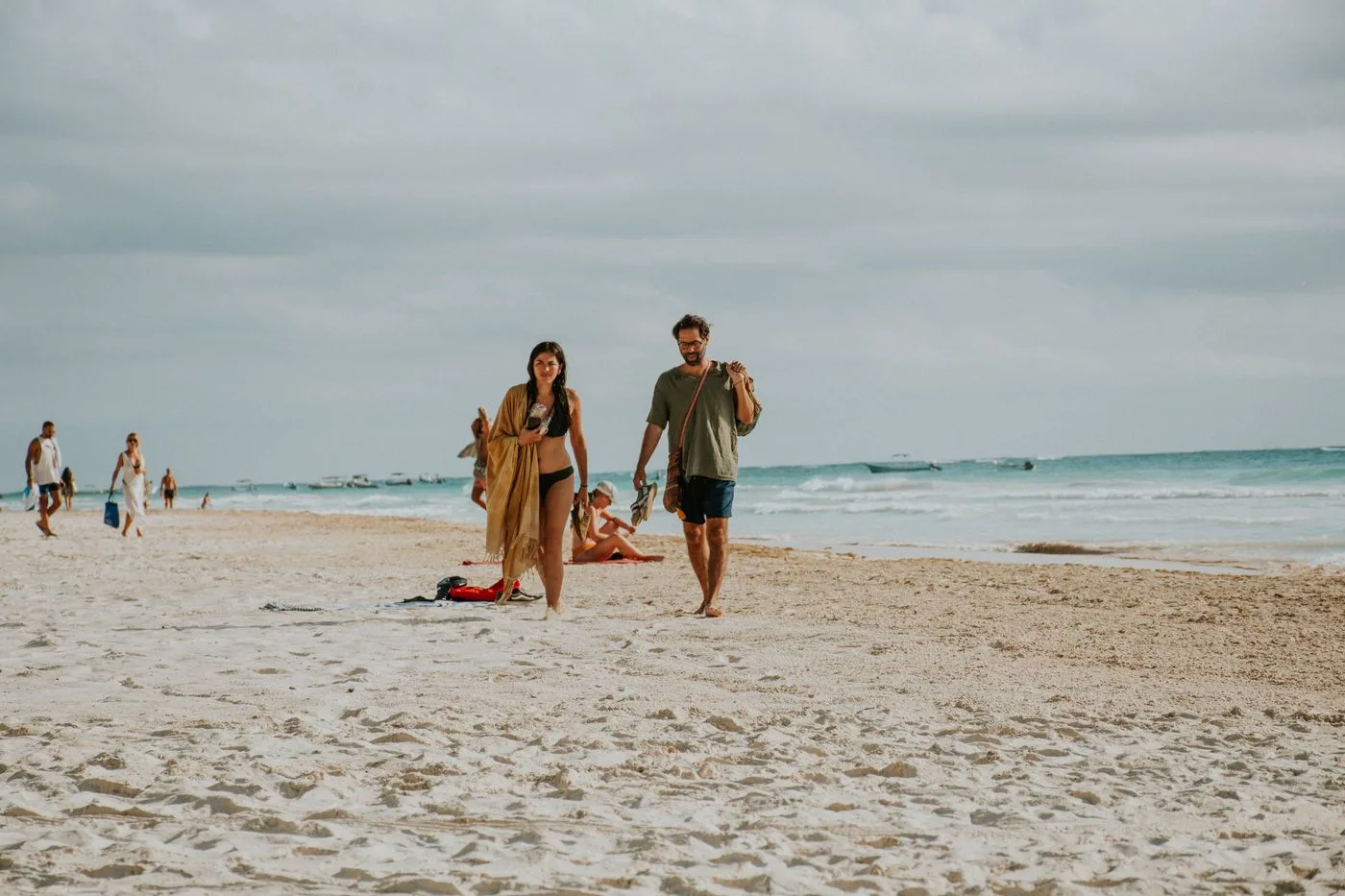 Couple walking on a sandy beach by the ocean during a sunny day, enjoying vacation and leisure.