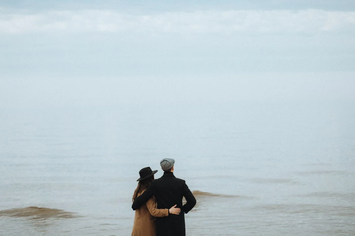 A couple affectionately embraces while gazing at the serene seashore horizon.