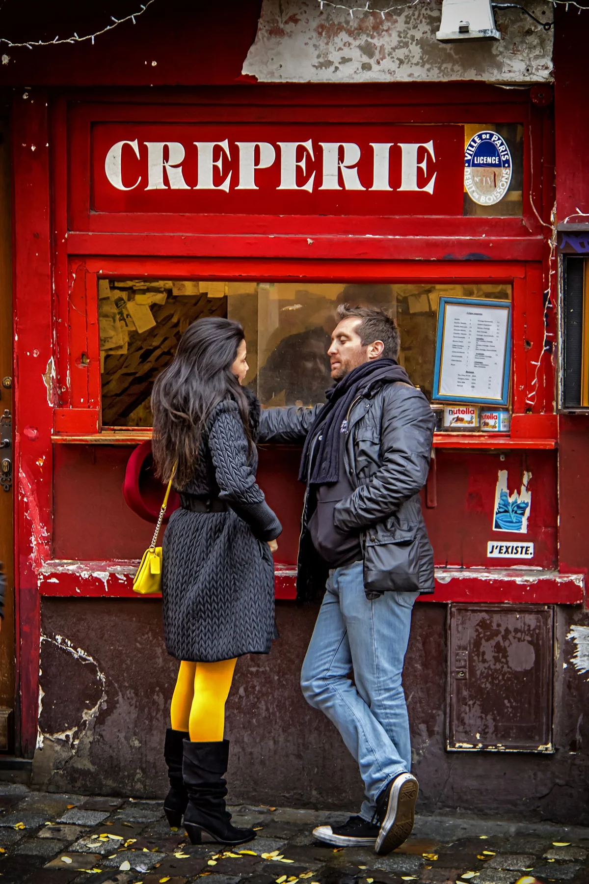 A couple conversing outside a vibrant creperie in Paris, showcasing urban fashion and city life.