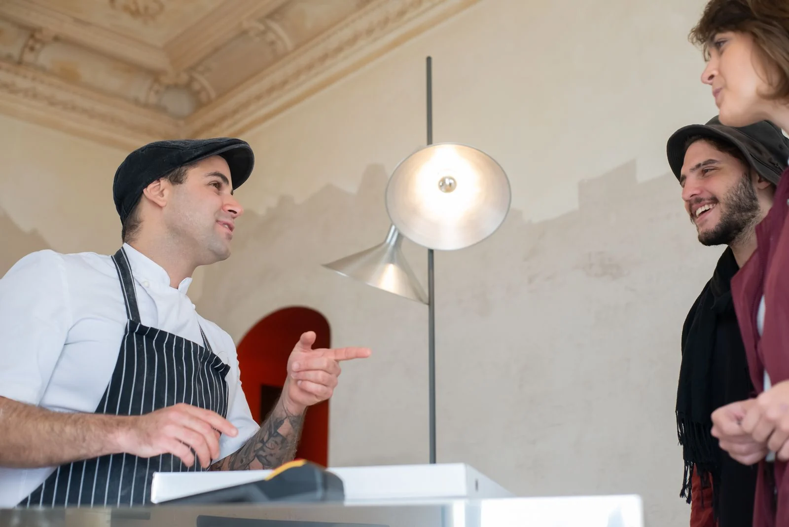 Chef in a stylish hat conversing with happy customers in a restaurant setting.