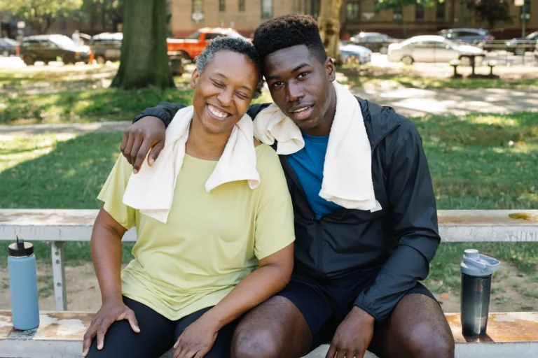A smiling couple relaxes on a park bench after exercising, embodying health and companionship.