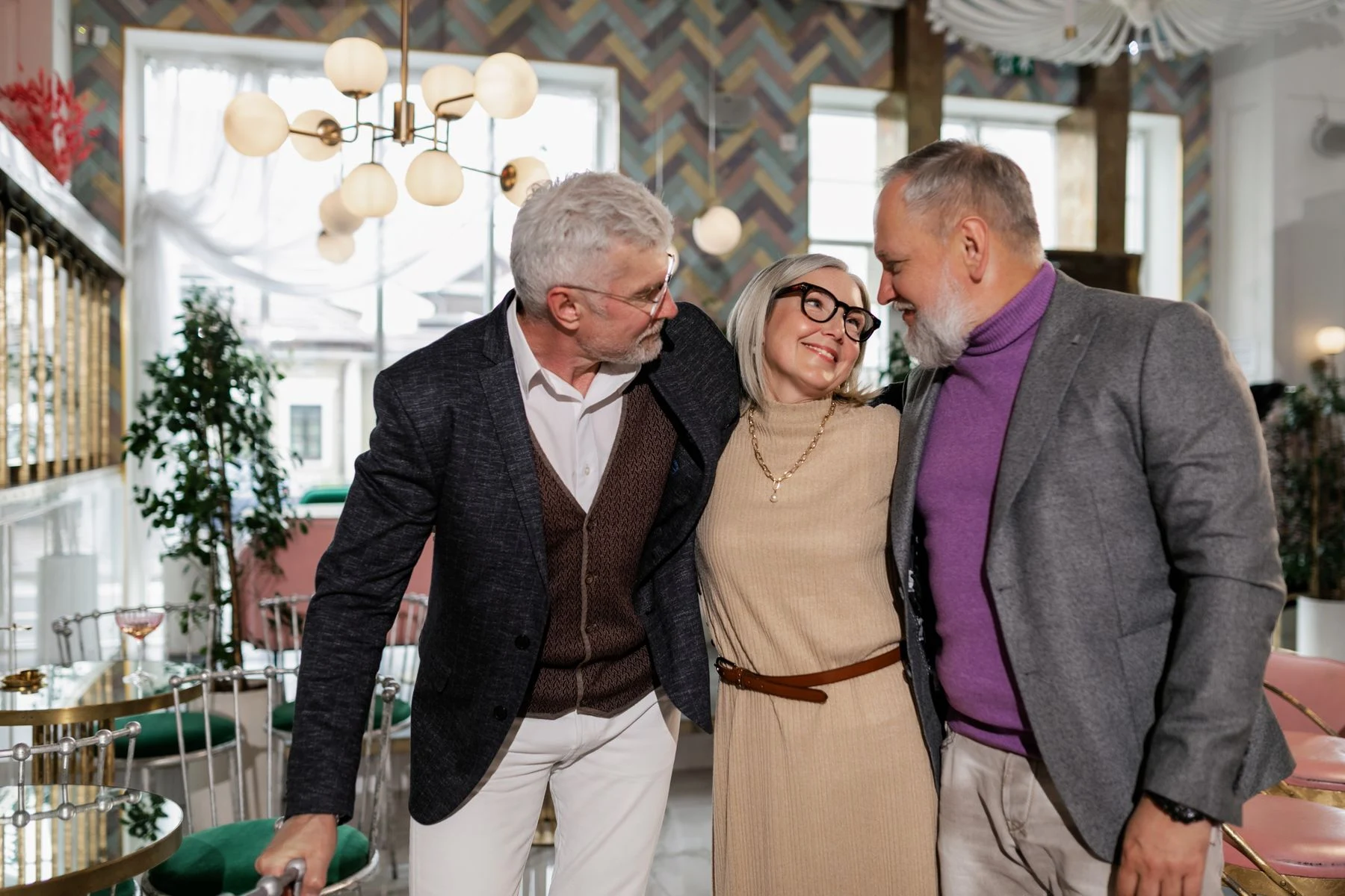 Three adults smiling with their arms around one another in a cafe