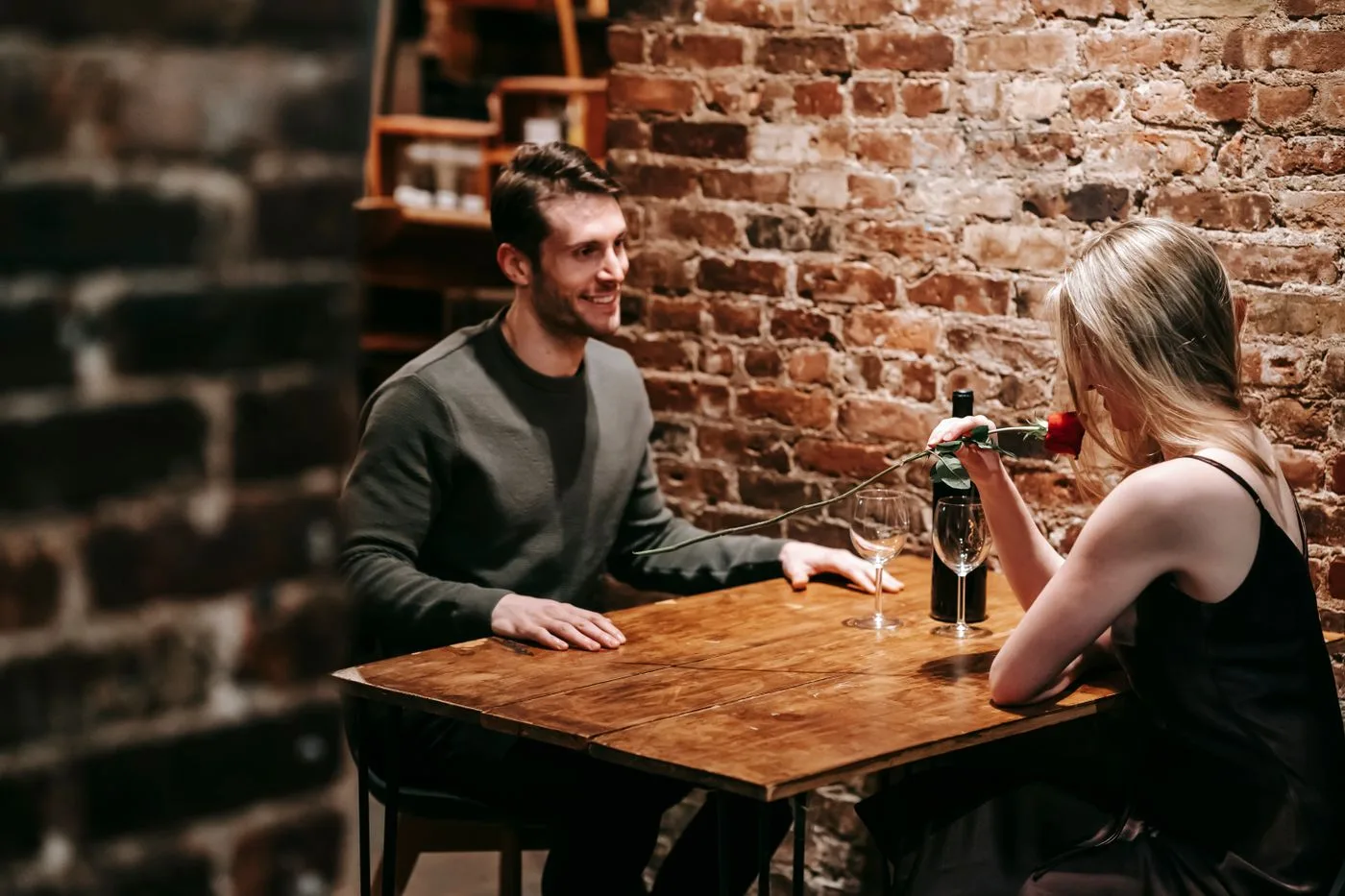 A couple enjoying a romantic dinner with rose and wine in a cozy restaurant setting.