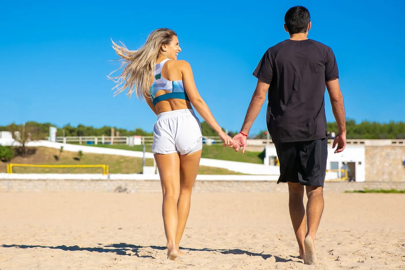 Couple holding hands and walking joyfully on a bright summer beach.