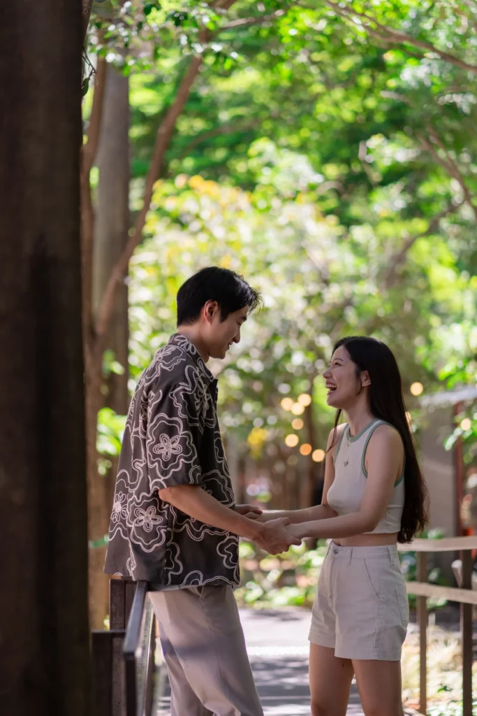 Happy couple laughing and holding hands in a lush green outdoor setting.