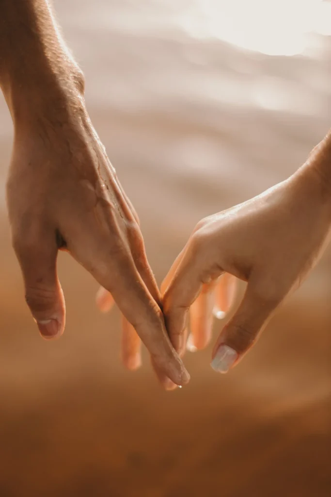 A close-up of a couple holding hands with a romantic sunset in the background.