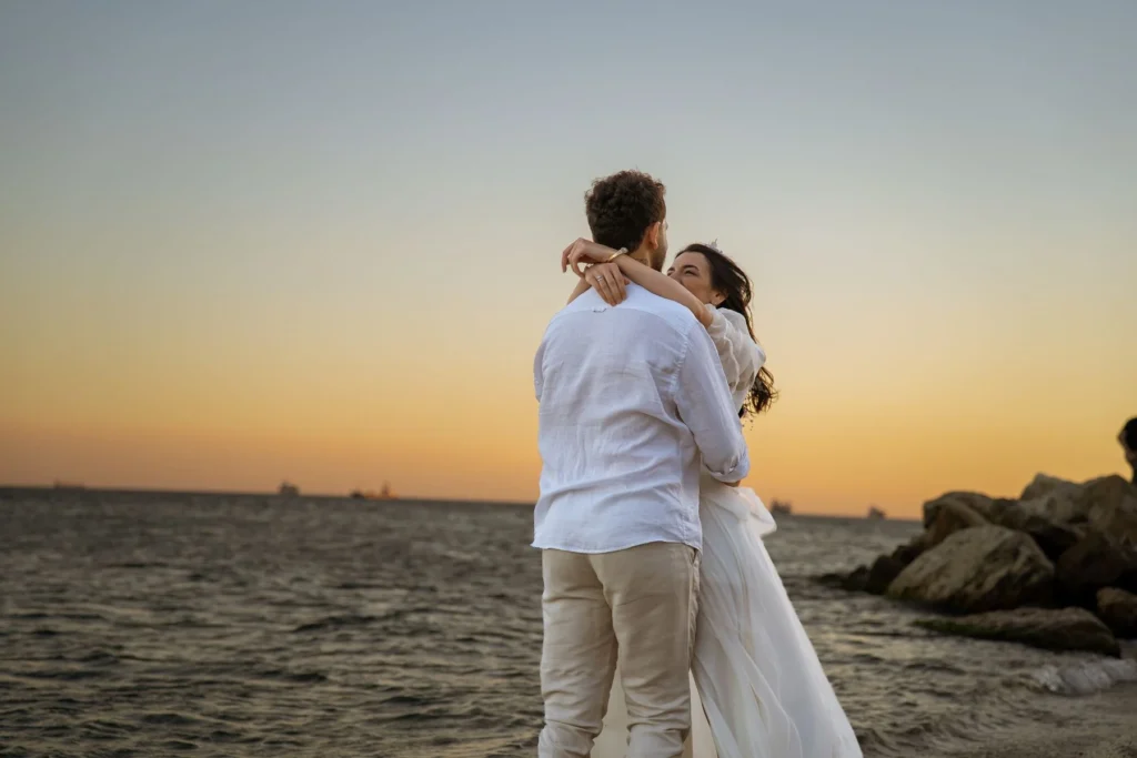 A couple in love embraces at the beach during a stunning sunset, creating a romantic moment.