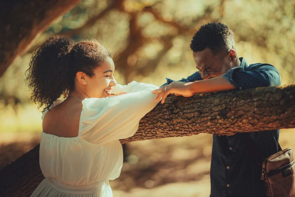 A happy couple enjoying a sunny day outdoors, laughing together by a tree.