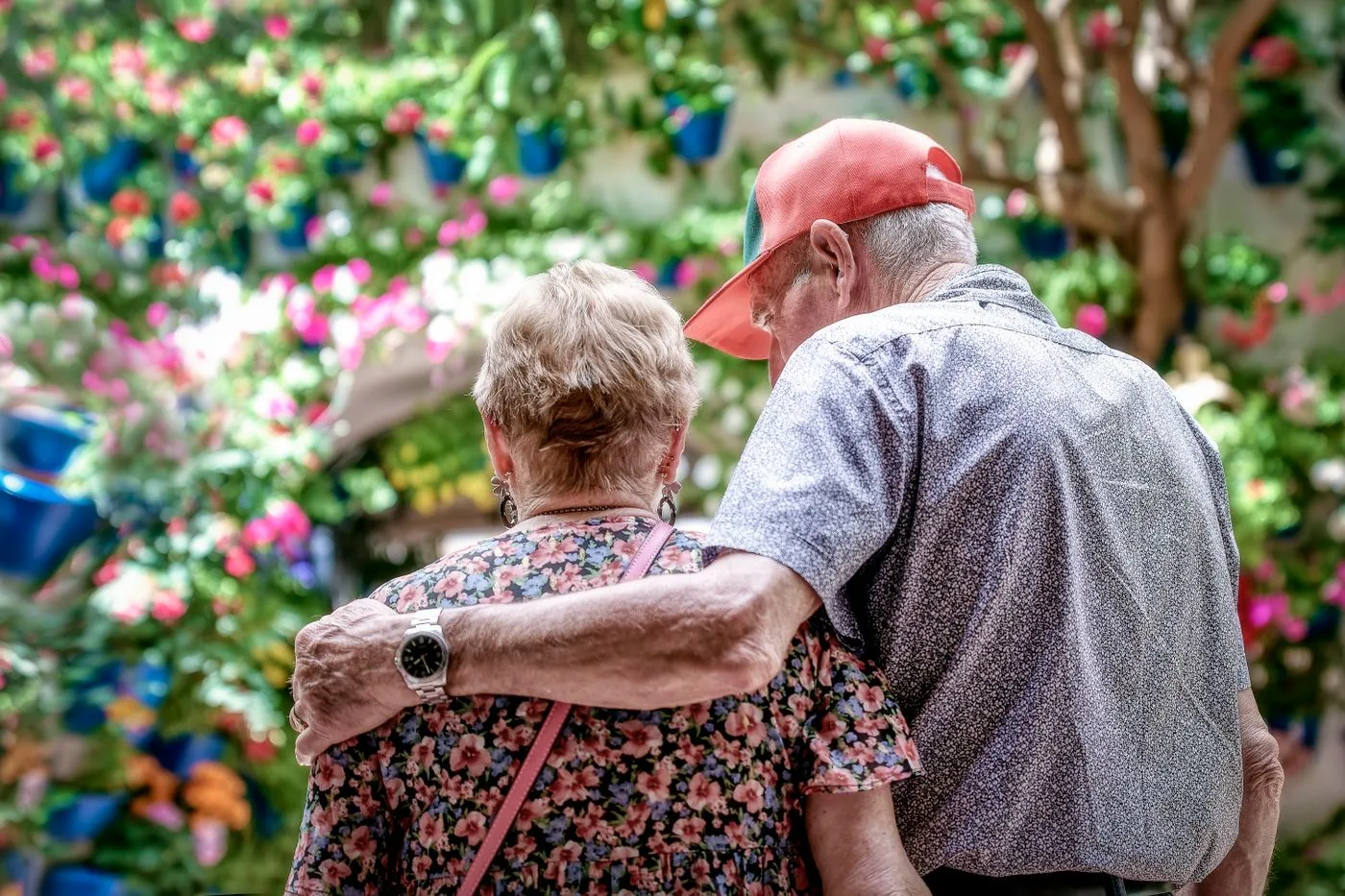 A loving senior couple embraces outdoors in a colorful garden in Córdoba, Spain.