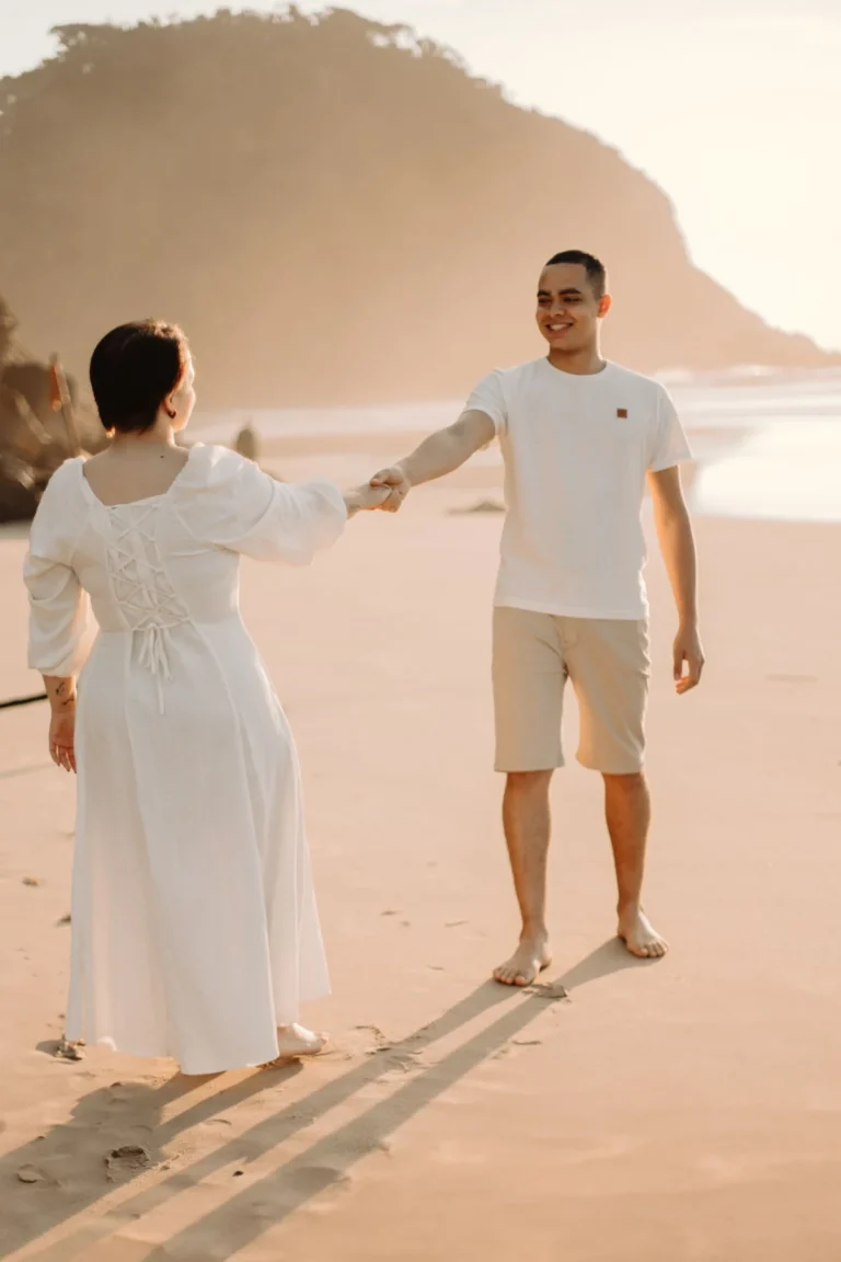 A couple holds hands on a serene beach during sunset, capturing a romantic moment.