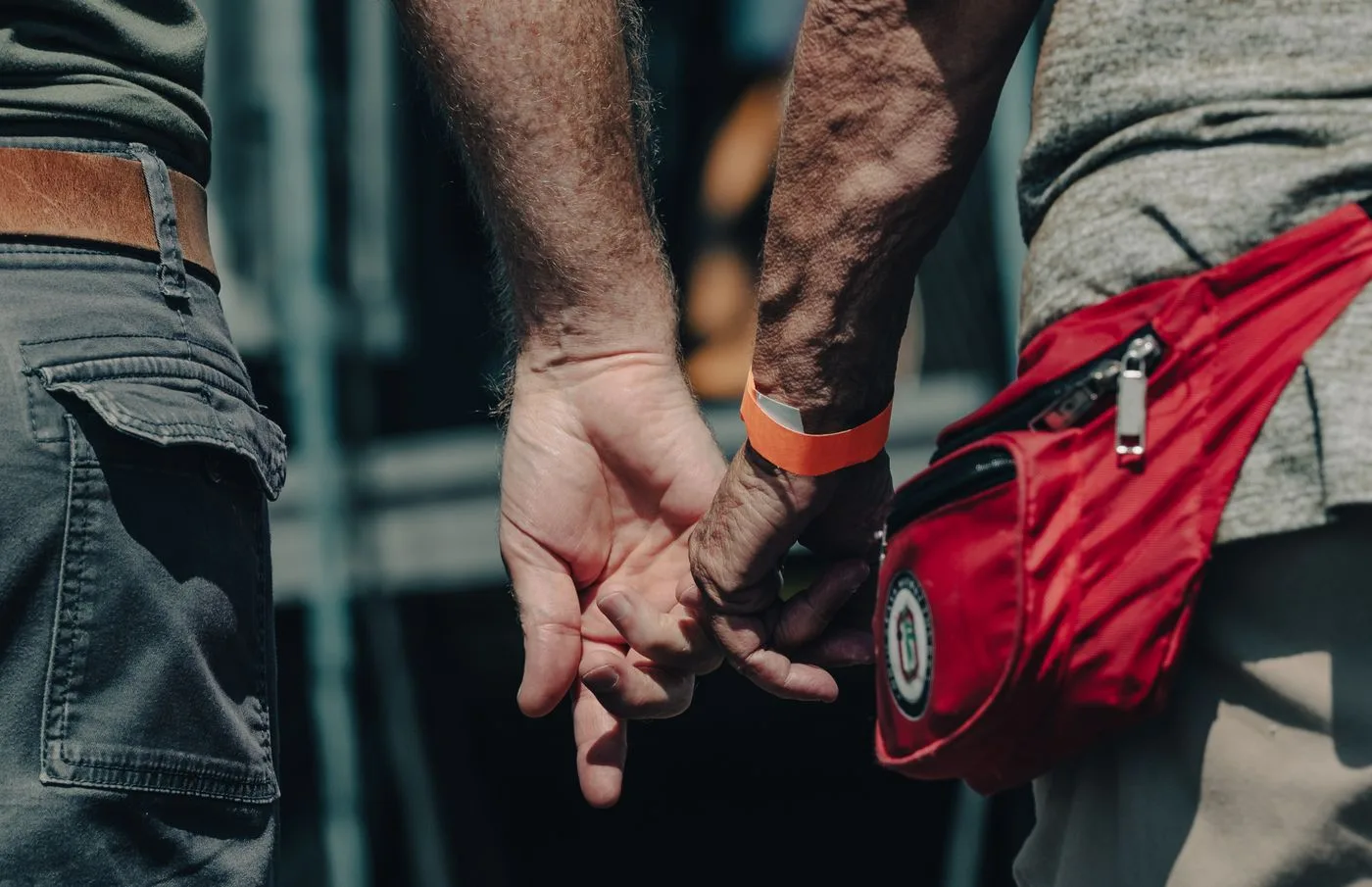 Close-up of two men in a couple holding hands outdoors, showcasing love and unity.