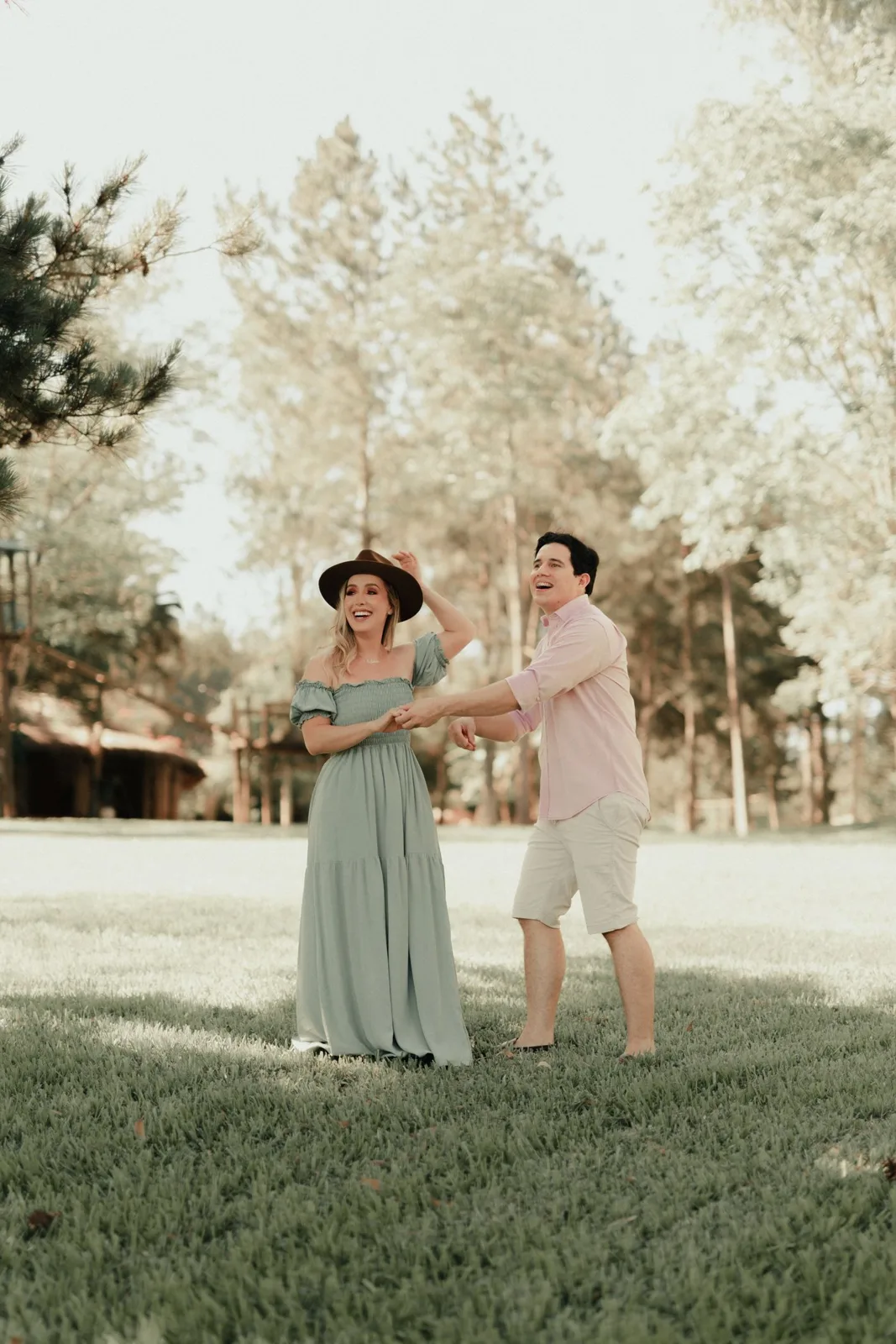 A happy couple laughing and having fun together in a serene park setting on a sunny day.