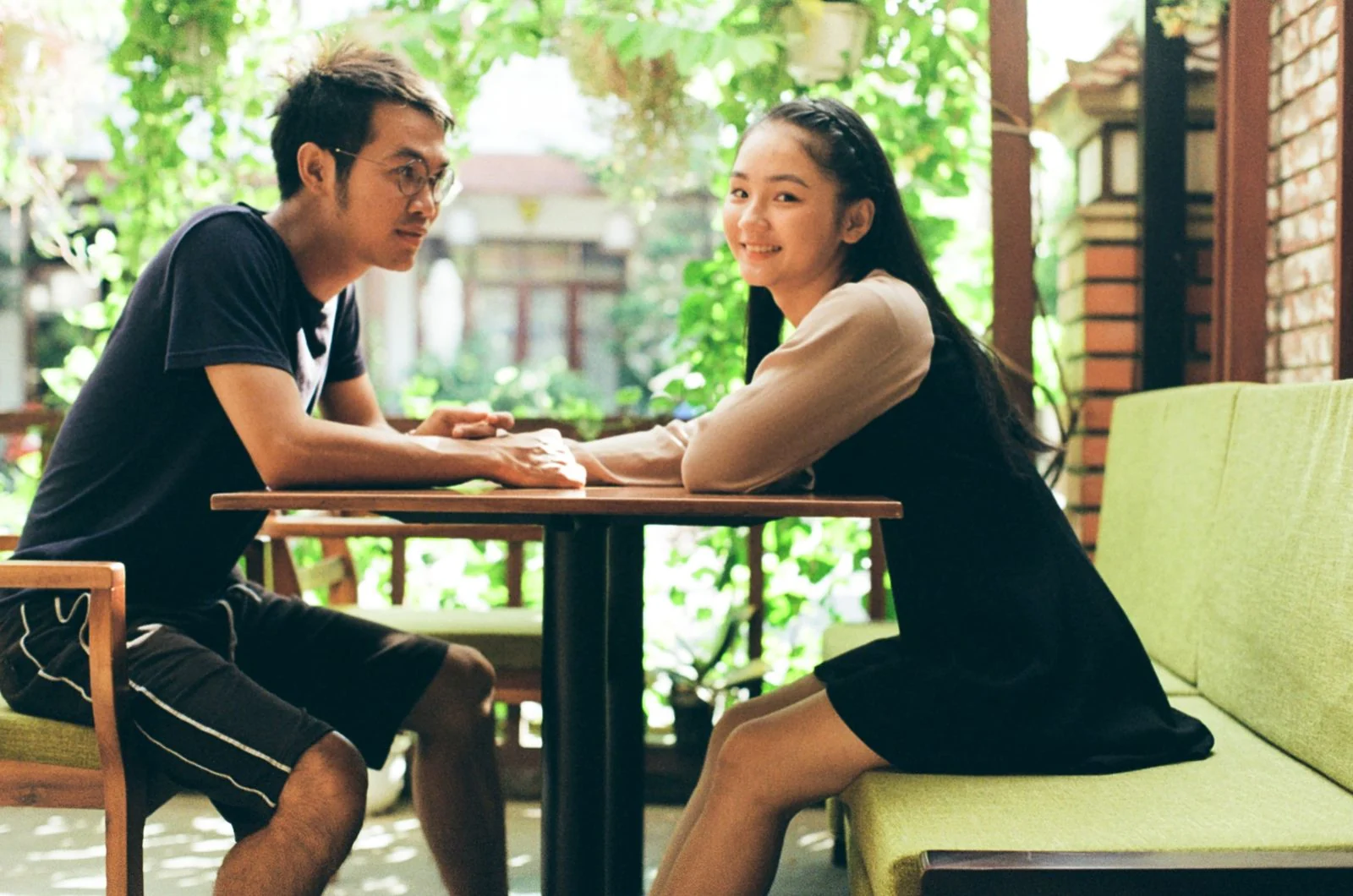 A young couple sitting together at an outdoor cafe table, enjoying each other's company.