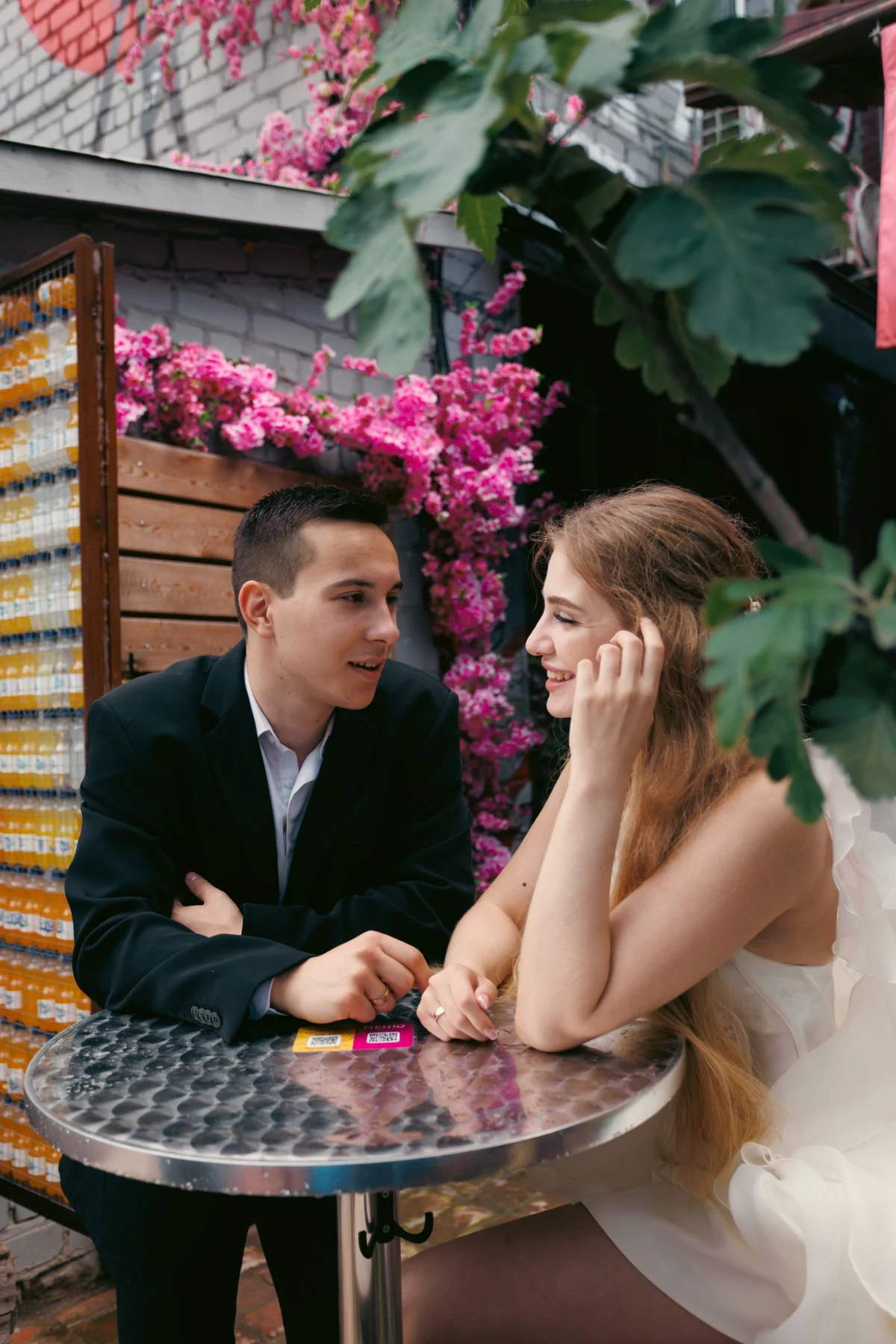 Couple enjoying a romantic outdoor café date surrounded by vibrant pink flowers.