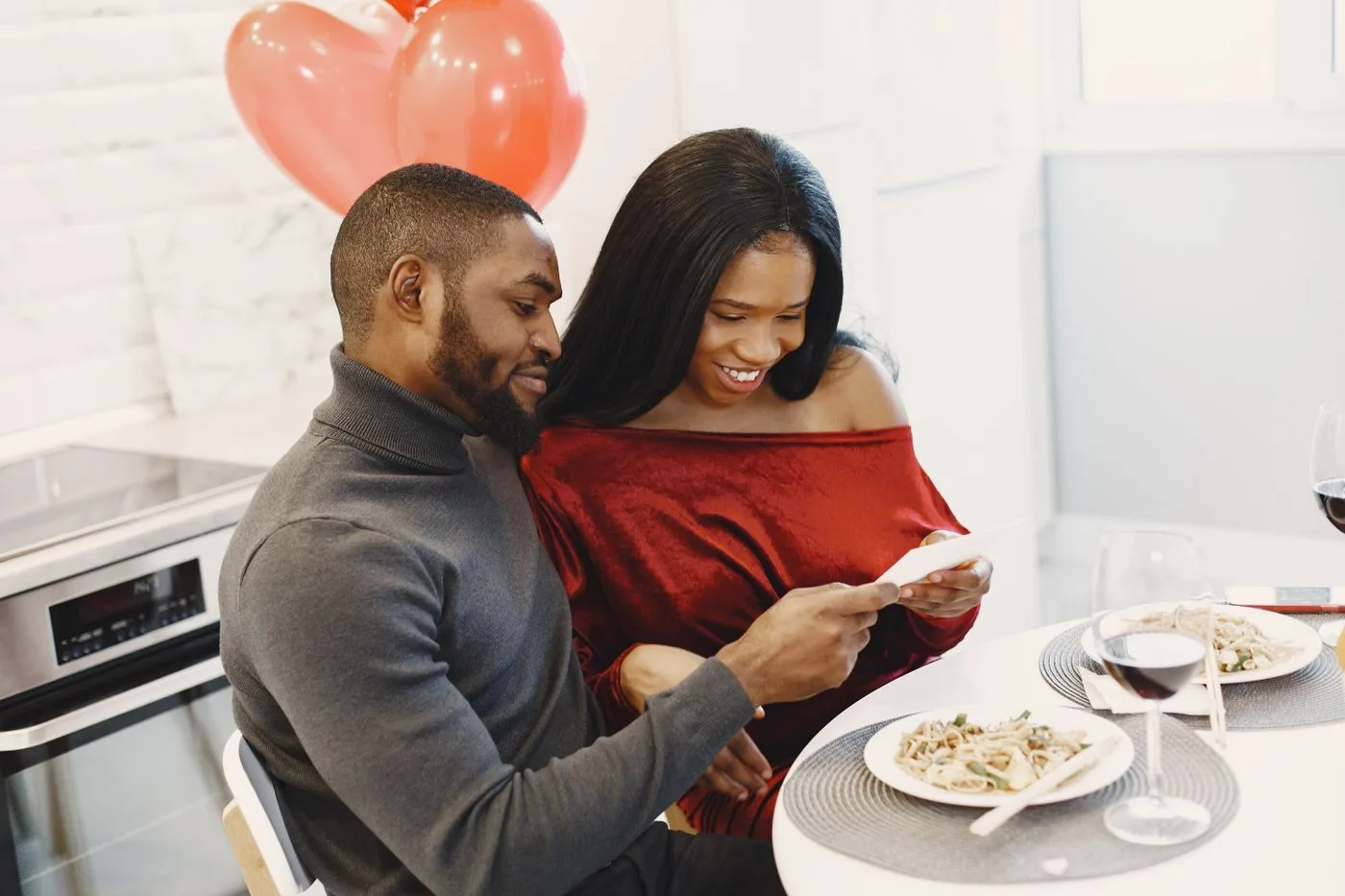 Couple enjoying a romantic dinner indoors with balloons and smiles.
