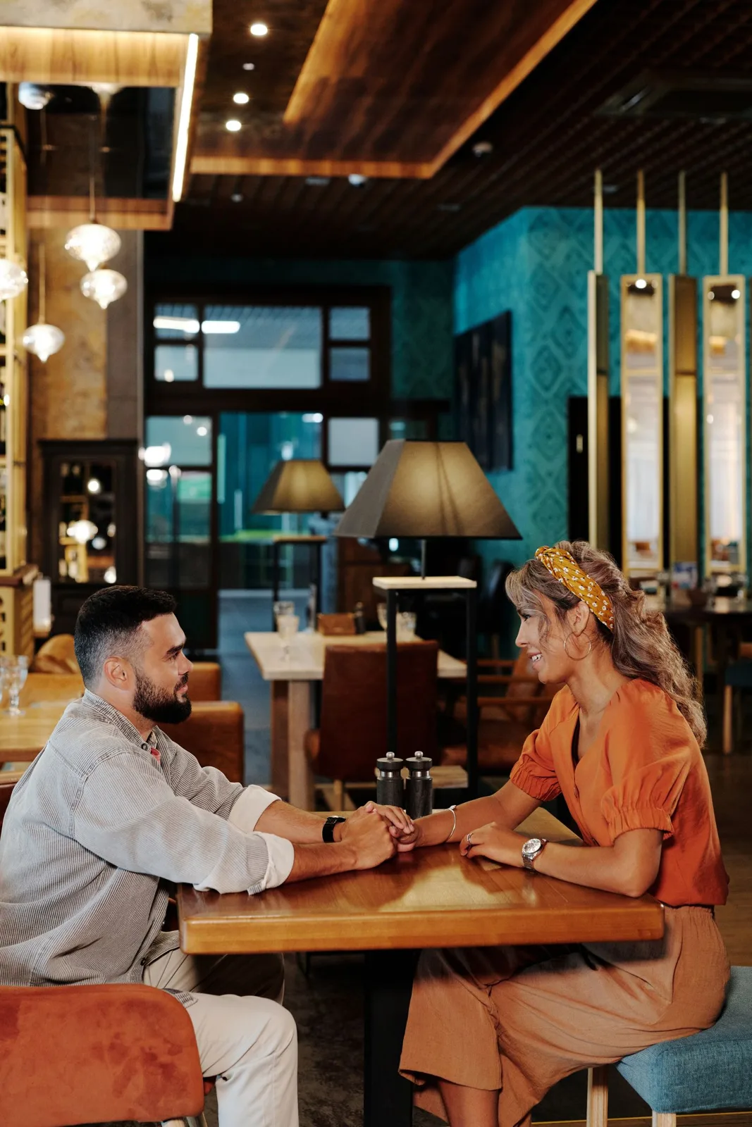 Smiling couple holding hands during a romantic dinner date in a cozy, well-decorated cafe.