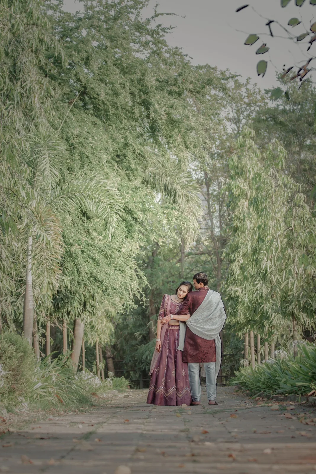 A loving couple embraces while strolling through a tree-lined path in a park.