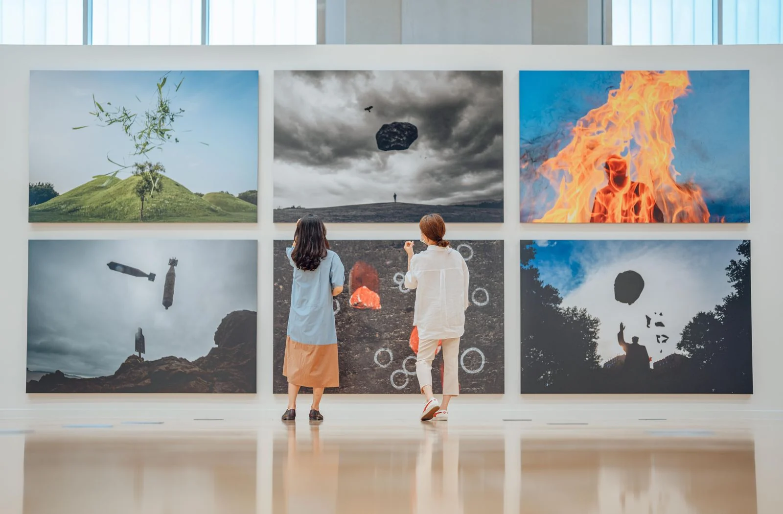 Two people observe various artworks in a modern art gallery setting.