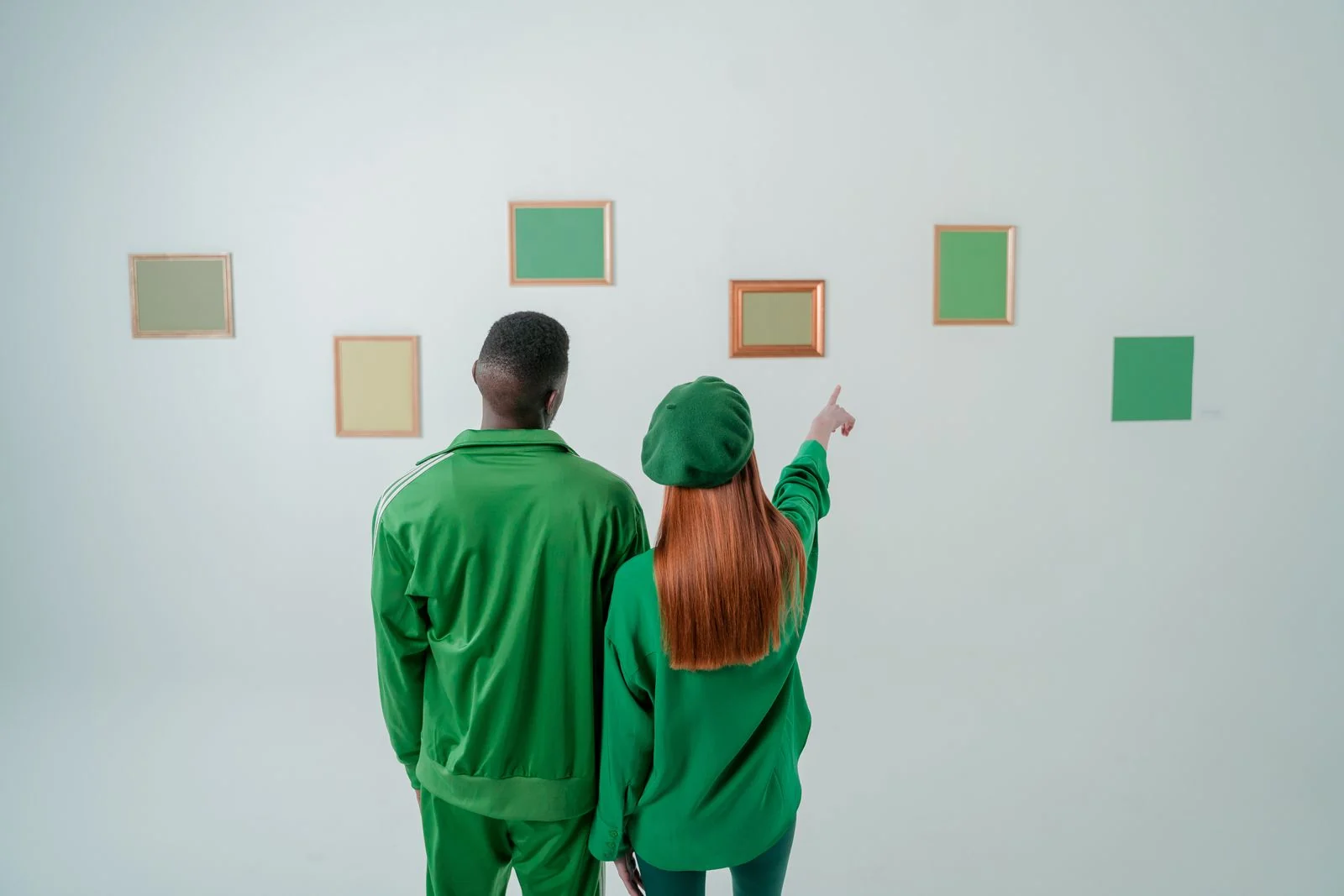 A couple exploring a minimalist art gallery with green-themed frames on the wall.