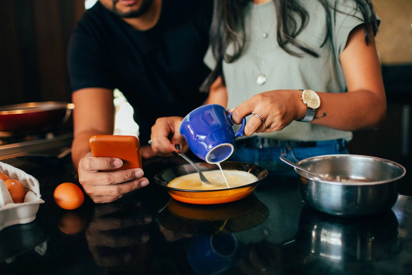 A couple prepares a meal together, pouring milk into a bowl, in a modern kitchen setting.