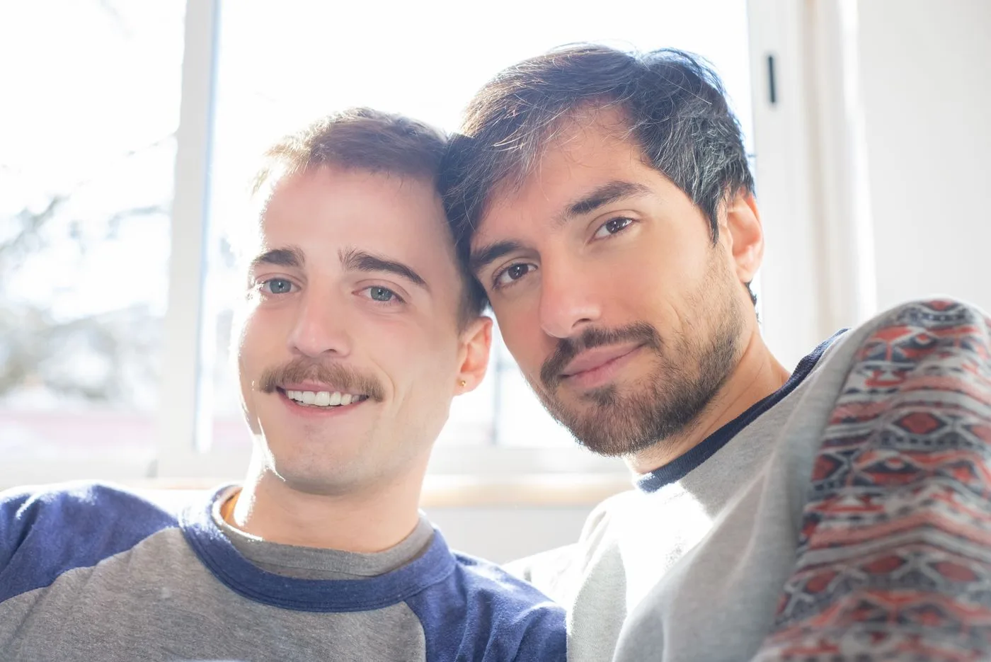 Two men embracing and smiling in a sunlit room, showcasing affection and togetherness.