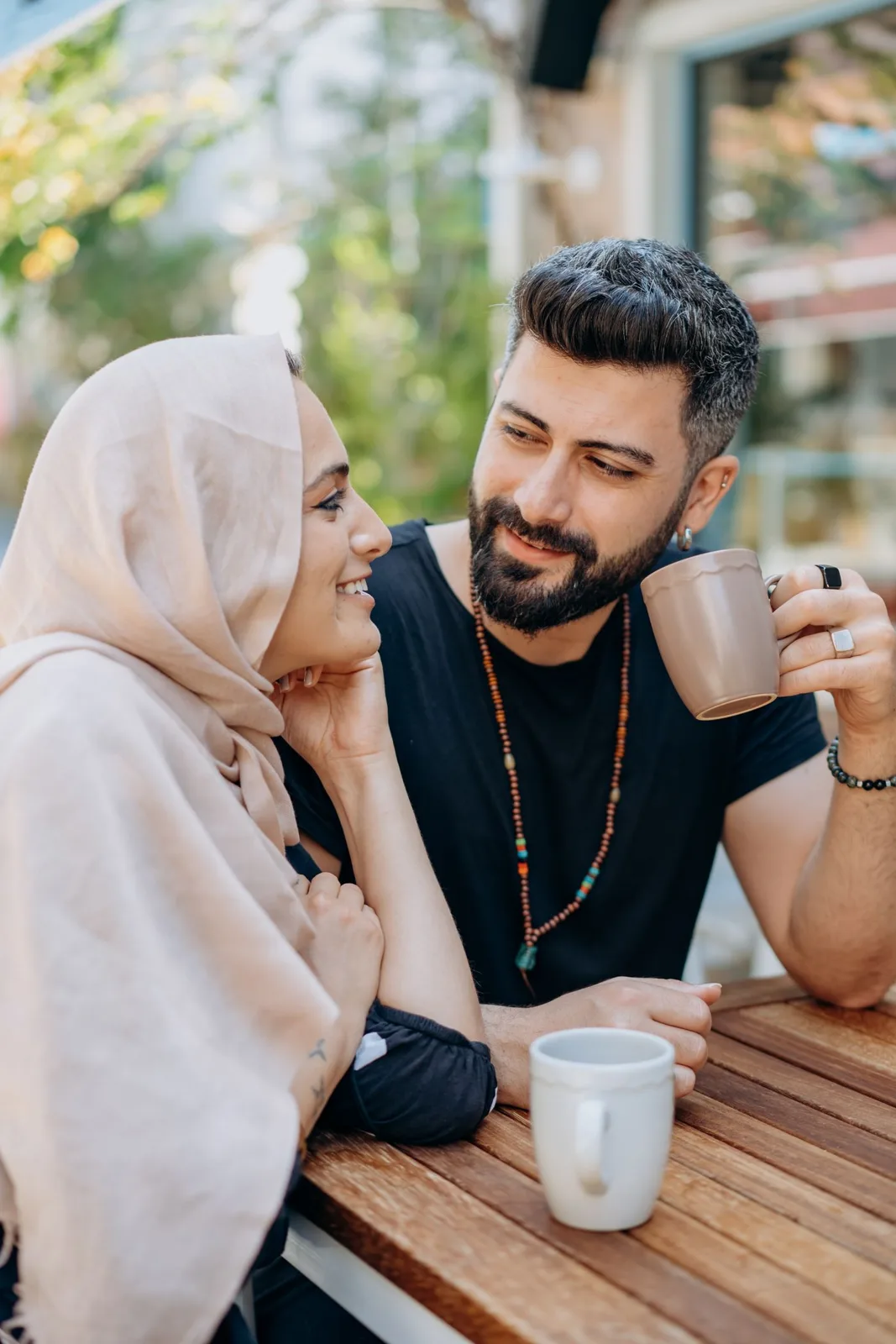 A loving couple shares a cozy moment with coffee outdoors, smiling and enjoying the day.