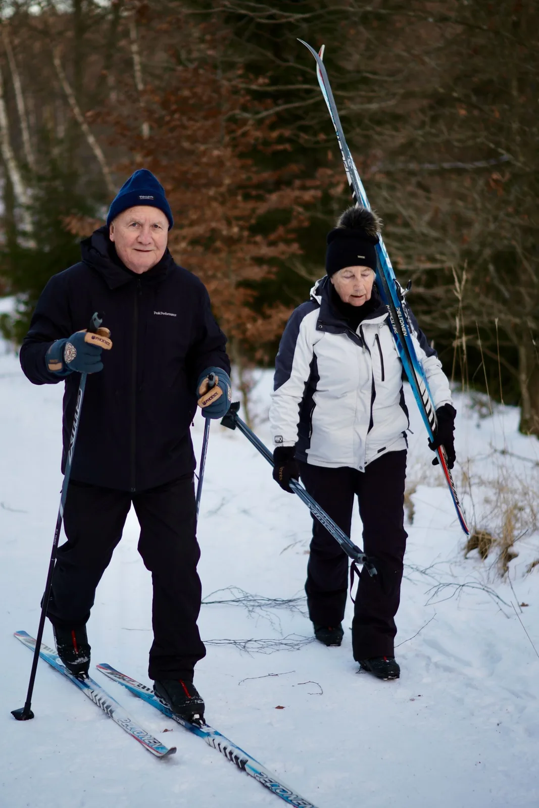 Active senior couple cross-country skiing in winter forest landscape, embracing outdoor lifestyle.