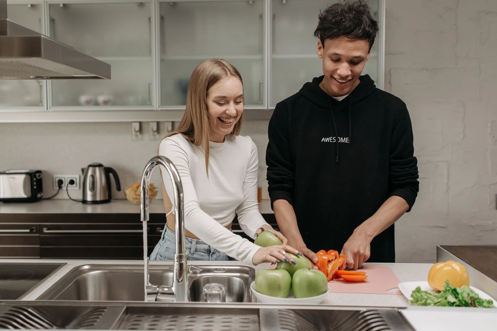 Smiling young couple cooking together in a modern kitchen, slicing fresh vegetables.