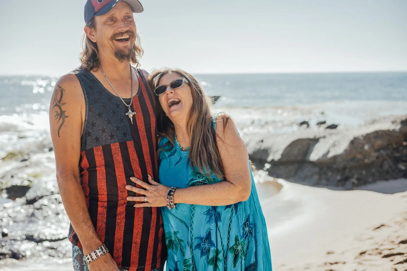 A cheerful couple laughing together at the sandy beach on a sunny day, showcasing happiness and togetherness.