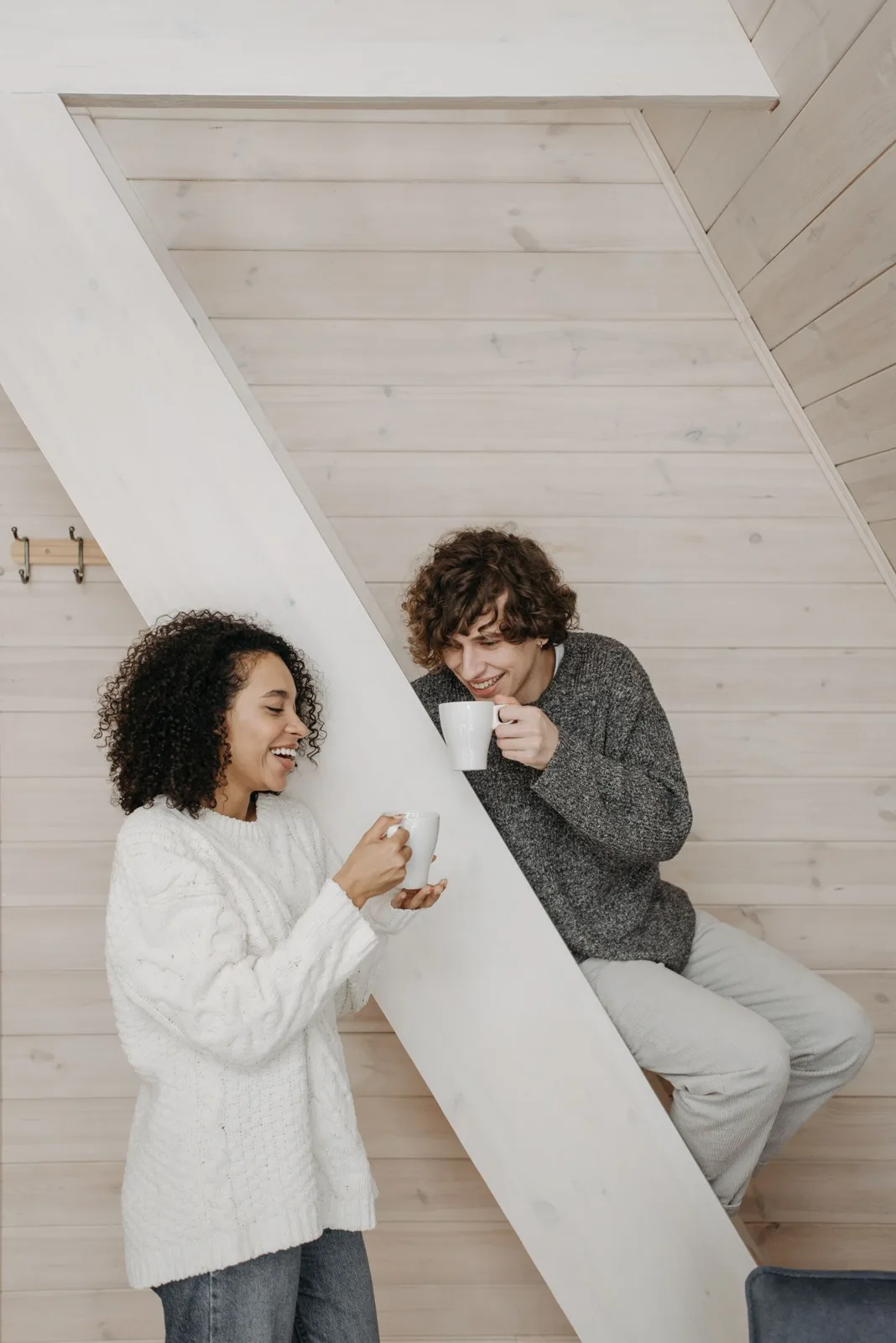 A joyful moment as a couple enjoys coffee together indoors, smiling and relaxed.
