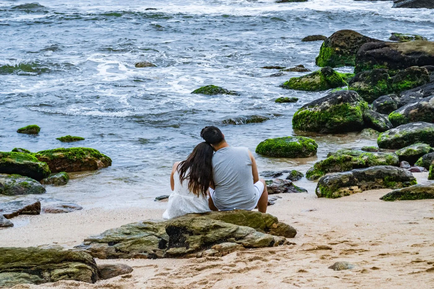 A couple enjoying a romantic moment on a rocky Brazilian beach with waves crashing nearby.